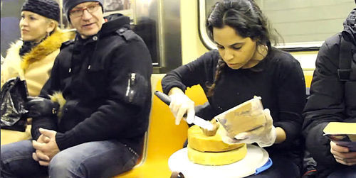 Banayan ices a two-layer cake on the train as fellow commuters look on. Still from video by Vanessa Turi (Parsons BFA Fine Art '13)